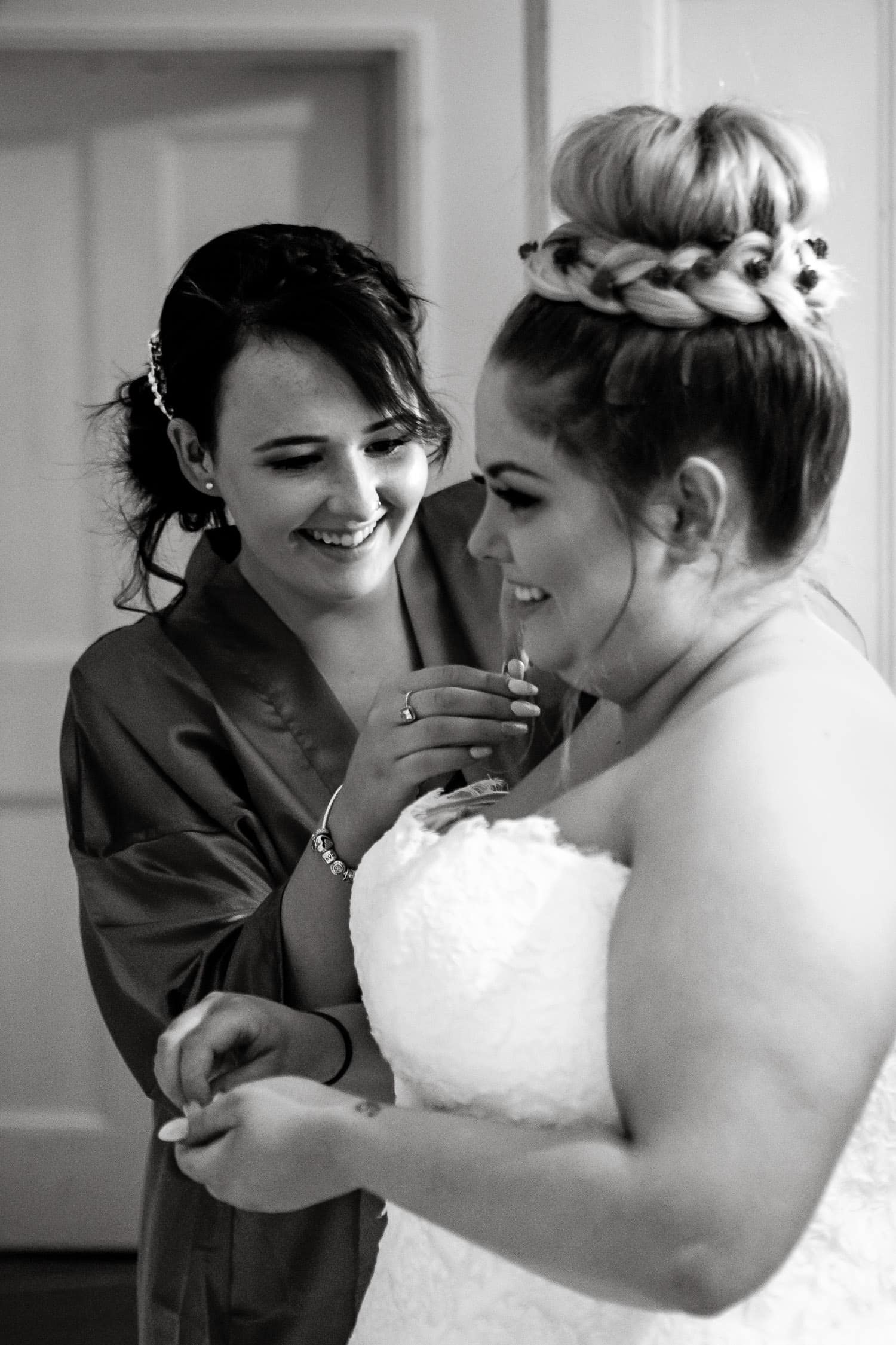 bride smiles while bridesmaid put on necklace by chapter one photography